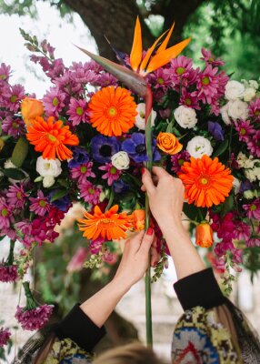 Papier peint  A girl with a red manicure holds a strelitzia against the background of floristic composition of bright multi-colored flowers.