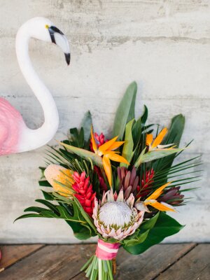 Papier peint  An exotic bouquet of tropical flowers: protea, red ginger, strelitzia, ficus, and palm leaves. Nearby is a decorative pink flamingo.