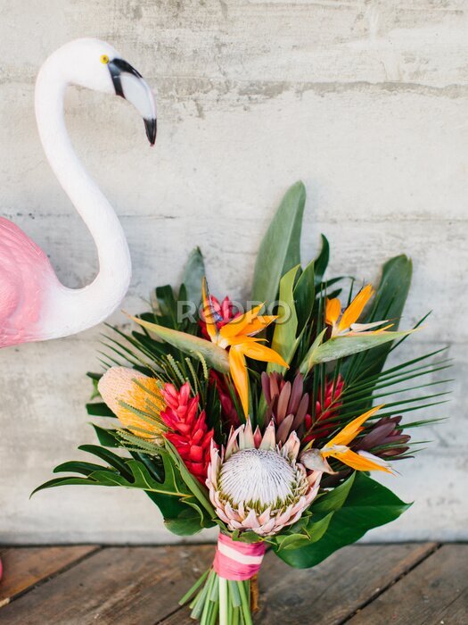 Papier peint  An exotic bouquet of tropical flowers: protea, red ginger, strelitzia, ficus, and palm leaves. Nearby is a decorative pink flamingo.
