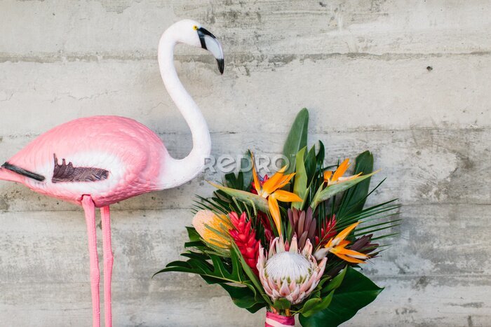 Papier peint  An exotic bouquet of tropical flowers: protea, red ginger, strelitzia, ficus, and palm leaves. Nearby is a decorative pink flamingo.