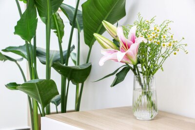 Papier peint  Beautiful bouquet of flowers (pink lilies along with small daisies) in glass vase on wooden surface besides a Giant White Bird of Paradise (Strelitzia nicolai), freshening and decorating home