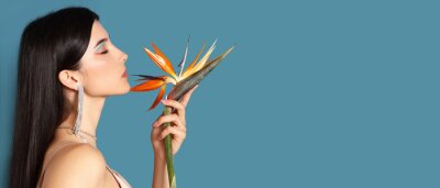 Papier peint  Beautiful young woman holding strelitzia flower on blue background with space for text