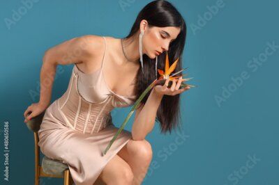Papier peint  Beautiful young woman with strelitzia flower sitting on chair against color background