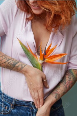 Papier peint  Belle fille aux cheveux rouges et un tatouage tient une fleur de strelitzia sur un fond bleu
