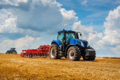 Papier peint  Blue new tractor with red harrow in the field against a cloudy sky, agricultural machinery work