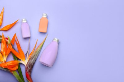 Papier peint  Bottles of cosmetic products and beautiful strelitzia flowers on lilac background with space for text