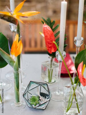 Papier peint  Bouquets of red anthurium, strelitzia, and tropical leaves stand in glass vases on a white table. There are white candles in the background. Tropical decor.