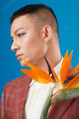 Papier peint  Calm or sad young man with eyeliner and rhinestones makeup holding strelitzia flower and looking away