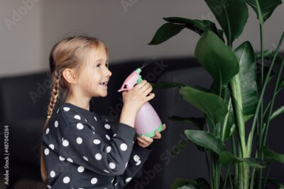 Papier peint  Cute caucasian little girl spraying Strelitzia houseplant from bottle, moisturising leaves during heating season at home. Greenery in modern apartment. Love and take care of plants, hobby time. Indoor