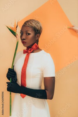 Papier peint  Fashion Shoot with african american woman in black gloves holding Strelitzia flower on beige and orange
