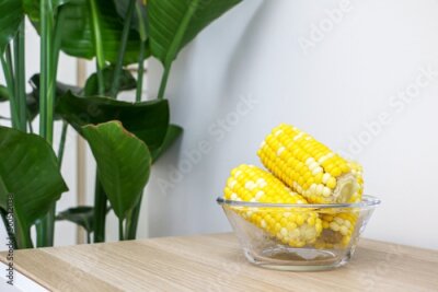 Papier peint  Glass bowl of corn on the cob (sweet corn, maize) on wooden surface besides Giant White Bird of Paradise Plant (Strelitzia nicolai), healthy living and healthy food concept