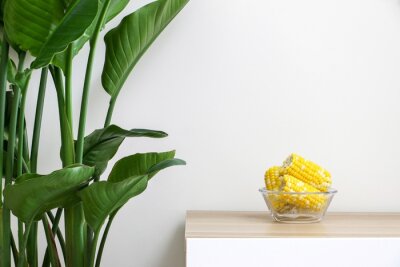 Papier peint  Glass bowl of corn on the cob (sweet corn, maize) on wooden table next to Giant White Bird of Paradise Plant (Strelitzia nicolai), healthy lifestyle and eating concept