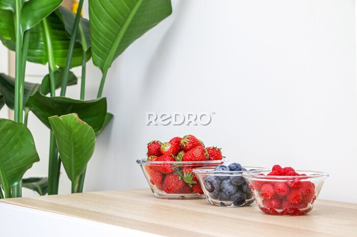 Papier peint  Glass bowls of strawberries, blueberries and raspberries on wooden surface besides a magnificent Giant White Bird of Paradise Plant (Strelitzia nicolai), for healthy living