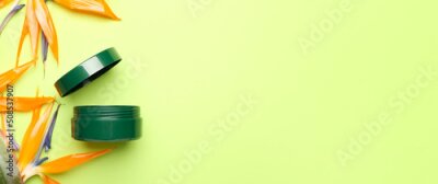 Papier peint  Jar of cosmetic cream and strelitzia flowers on green background with space for text
