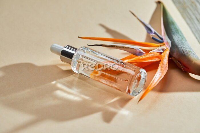 Papier peint  Liquid gel or serum in a glass transparent bottle with dropper and Bird of Paradise flower (Strelitzia reginae) on a beige background