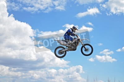 Papier peint  Motocross rider standing on the motorcycle MX is flying over the hill on a background of blue sky