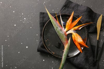 Papier peint  Plate with beautiful strelitzia flower, napkin and knife on black grunge background