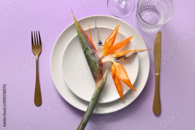 Papier peint  Plates with beautiful strelitzia flower and cutlery on lilac background