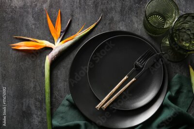 Papier peint  Plates with beautiful strelitzia flower, glasses and cutlery on grunge black background