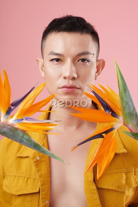 Papier peint  Portrait of young man wearing eyeliner and rhinestones makeup when standing among strelitzia flowers