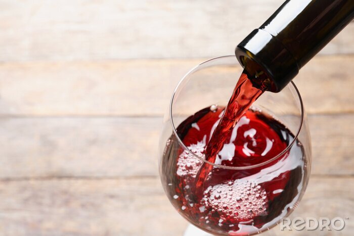 Papier peint  Pouring red wine from bottle into glass on blurred background, closeup. Space for text