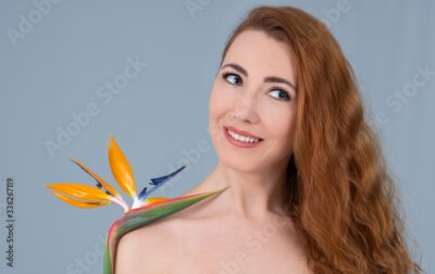 Papier peint  Redhead woman with blue eyes holding a strelitzia flower. Isolated on grey background. 