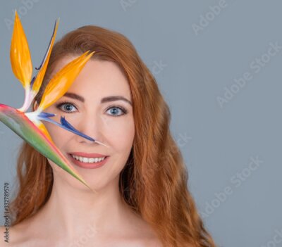 Papier peint  Redhead woman with blue eyes holding a strelitzia flower. Isolated on grey background. 