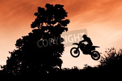Papier peint  Statut des silhouate saut de motocross sur la lumière ambrée du coucher de soleil fond.