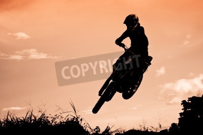 Papier peint  Statut des silhouate saut de motocross sur la lumière ambrée du coucher de soleil fond.