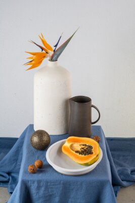 Papier peint  Still life on a blue table: papaya, strelitzia flower
