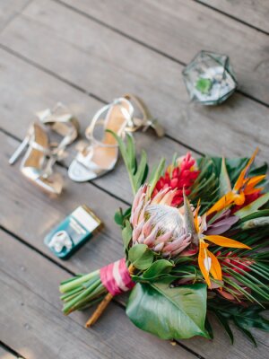Papier peint  The bride's bouquet in a tropical style with exotic flowers lies on a wooden floor. Bouquet of protea, palm leaves, strelitzia, and red ginger. In the background are women's shoes.