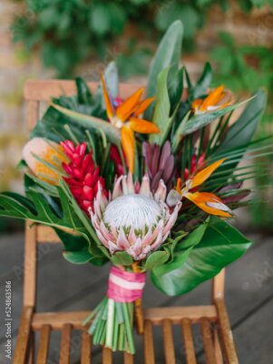 Papier peint  The bride's bouquet in a tropical style with exotic flowers stands on a wooden chair. Bouquet of protea, palm leaves, strelitzia, and red ginger.