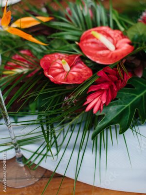 Papier peint  The decor of tropical flowers on the questionnaire table. Red anthurium, palm leaves, red ginger, strelitzia.