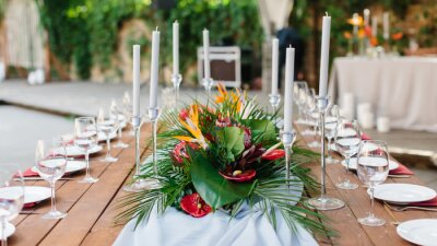 Papier peint  Wedding banquet decor in tropical style. In the center of the table is a white tablecloth, a bouquet of strelitzia, red anthurium, and tropical leaves. On the sides are candles, wine glasses, plates.