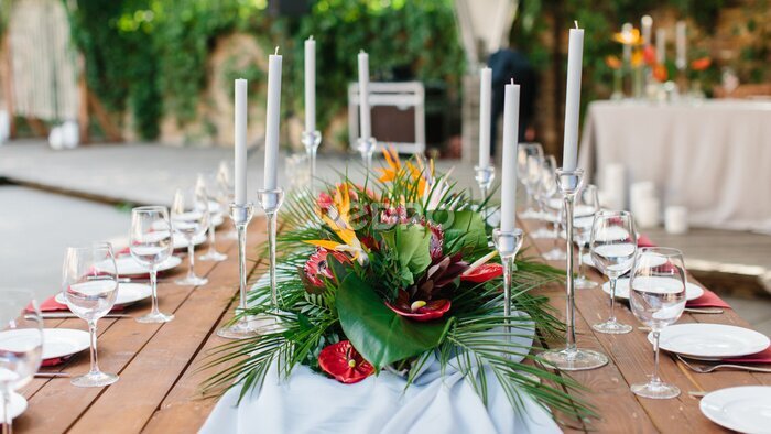Papier peint  Wedding banquet decor in tropical style. In the center of the table is a white tablecloth, a bouquet of strelitzia, red anthurium, and tropical leaves. On the sides are candles, wine glasses, plates.