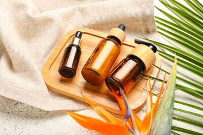 Papier peint  Wooden board with bottles of cosmetic products, strelitzia flower and palm leaf on light background