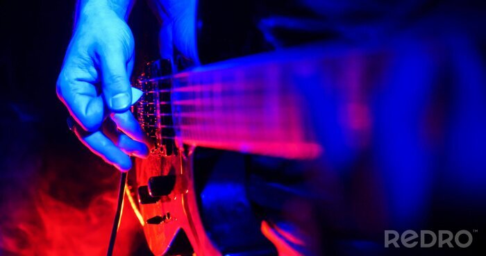 Poster  Concert de rock. Le guitariste joue de la guitare. La guitare est illuminée par des néons lumineux. Se concentrer sur les mains