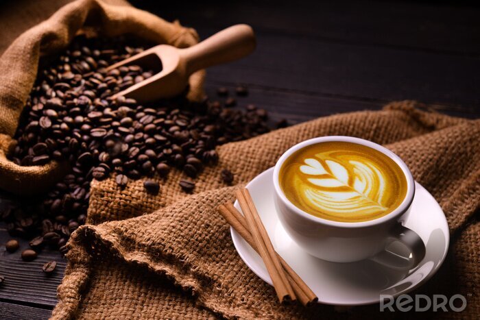 Poster  Cup of coffee latte and coffee beans in burlap sack on old wooden background