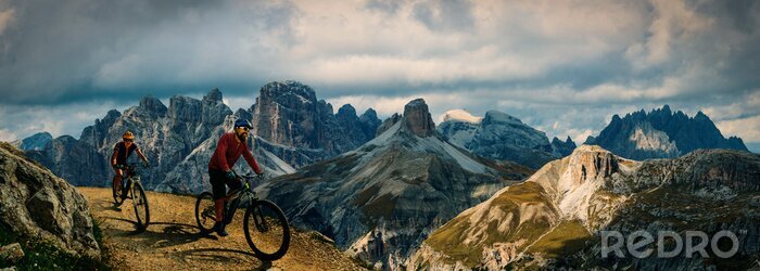 Poster  Cycling outdoor adventure in Dolomites. Cycling woman and man  on electric mountain bikes in Dolomites landscape. Couple cycling MTB enduro trail track. Outdoor sport activity.
