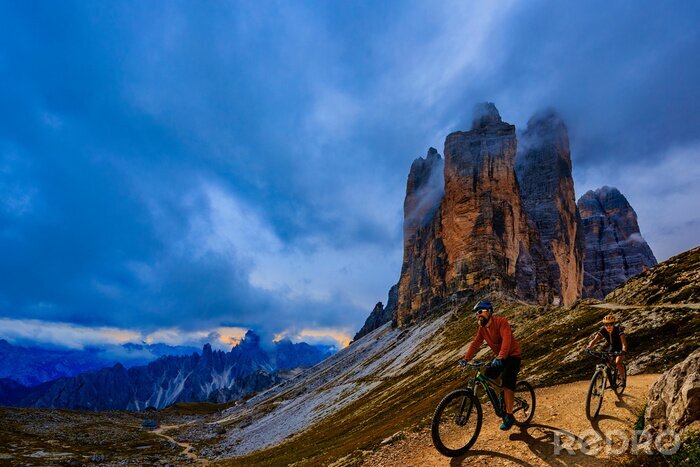 Poster  Cycling outdoor adventure in Dolomites. Cycling woman and man  on electric mountain bikes in Dolomites landscape. Couple cycling MTB enduro trail track. Outdoor sport activity.