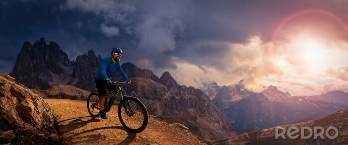 Poster  Cycling outdoor adventure. Man cycling on electric bike, rides mountain trail. Man riding on bike in Dolomites mountains landscape. Cycling e-mtb enduro trail track. Outdoor sport activity.