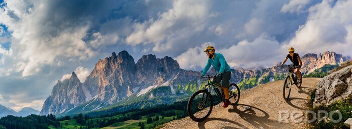 Poster  Cycling woman and man riding on bikes in Dolomites mountains andscape. Couple cycling MTB enduro trail track. Outdoor sport activity.