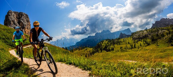 Poster  Cycling woman and man riding on bikes in Dolomites mountains landscape. Couple cycling MTB enduro trail track. Outdoor sport activity.