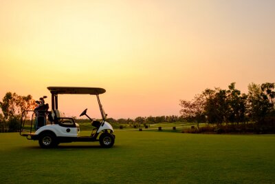 Poster  Golf cart car in fairway of golf course with fresh green grass field and cloud sky and tree  on sunset time