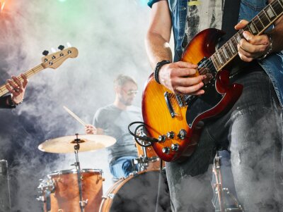Poster  Le groupe de rock joue sur scène. Guitariste, guitare basse et batterie. Guitariste au premier plan. Fermer.