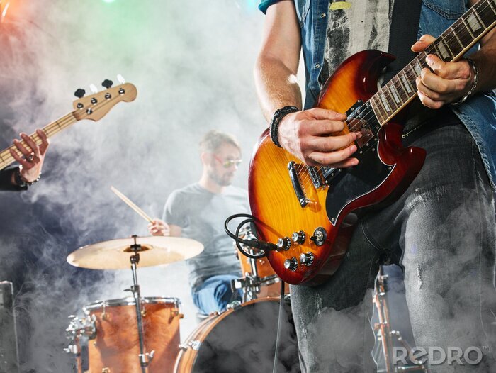 Poster  Le groupe de rock joue sur scène. Guitariste, guitare basse et batterie. Guitariste au premier plan. Fermer.