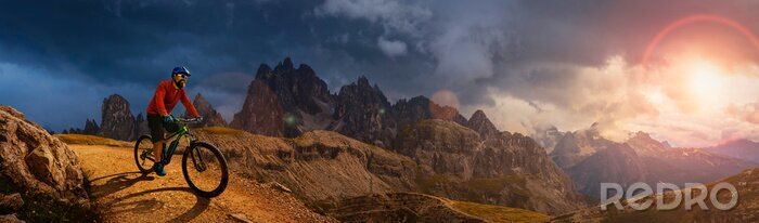 Poster  Man cycling on electric bike, rides mountain trail. Man riding on bike in Dolomites mountains landscape. Cycling e-mtb enduro trail track. Outdoor sport activity.