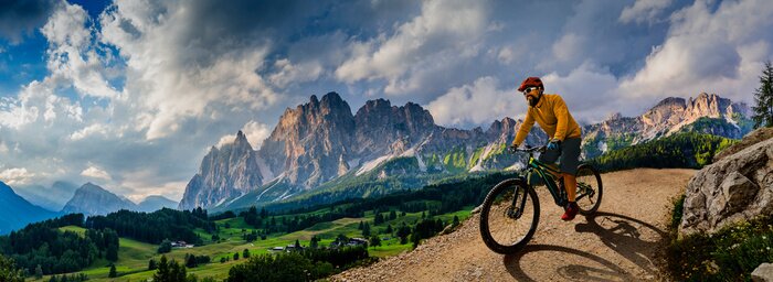 Poster  Man cycling on electric bike, rides mountain trail. Man riding on bike in Dolomites mountains landscape. Cycling e-mtb enduro trail track. Outdoor sport activity.