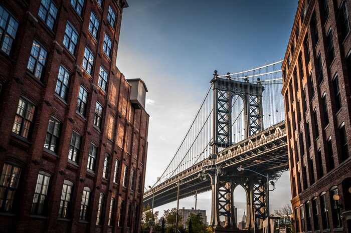 Poster  Manhattan Bridge vu depuis une ruelle étroite délimitée par deux bâtiments de brique sur une journée ensoleillée en été
