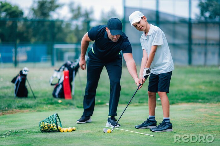 Poster  Personal golf lesson. Golf instructor with young boy on a golf driving range.
